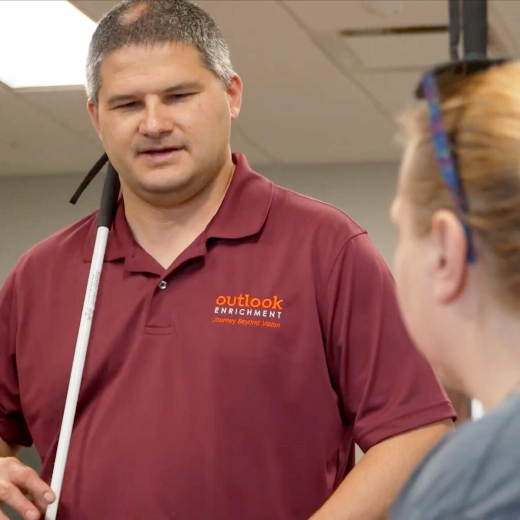 Man wearing a maroon shirt holds a cane while talking to a woman